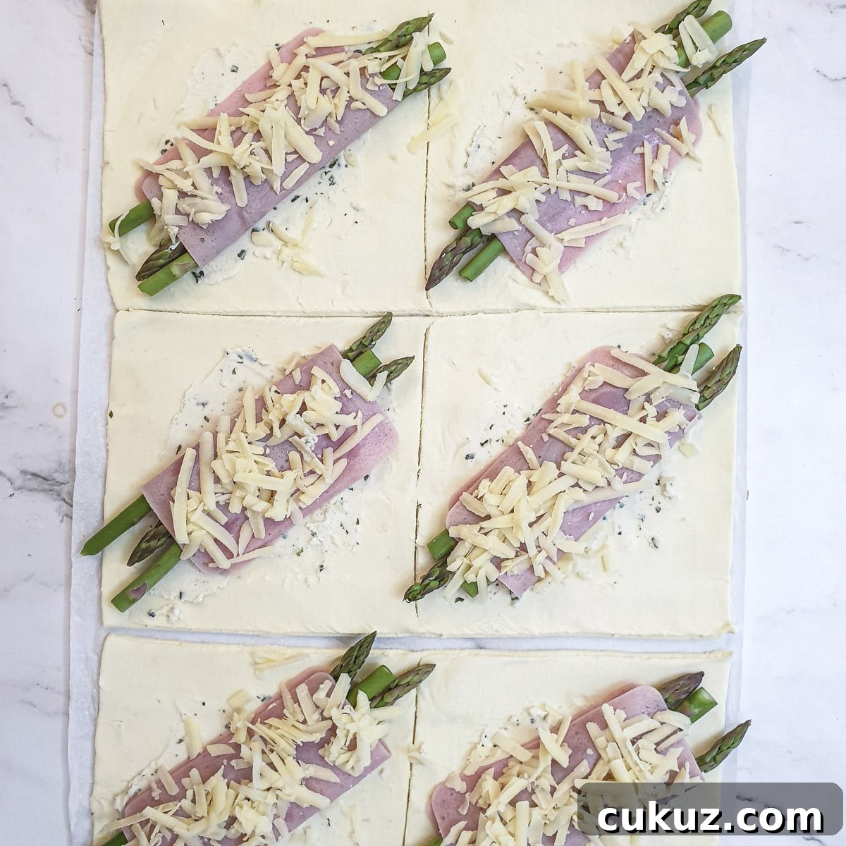 Grated cheese sprinkled over the ham and asparagus on the puff pastry squares.