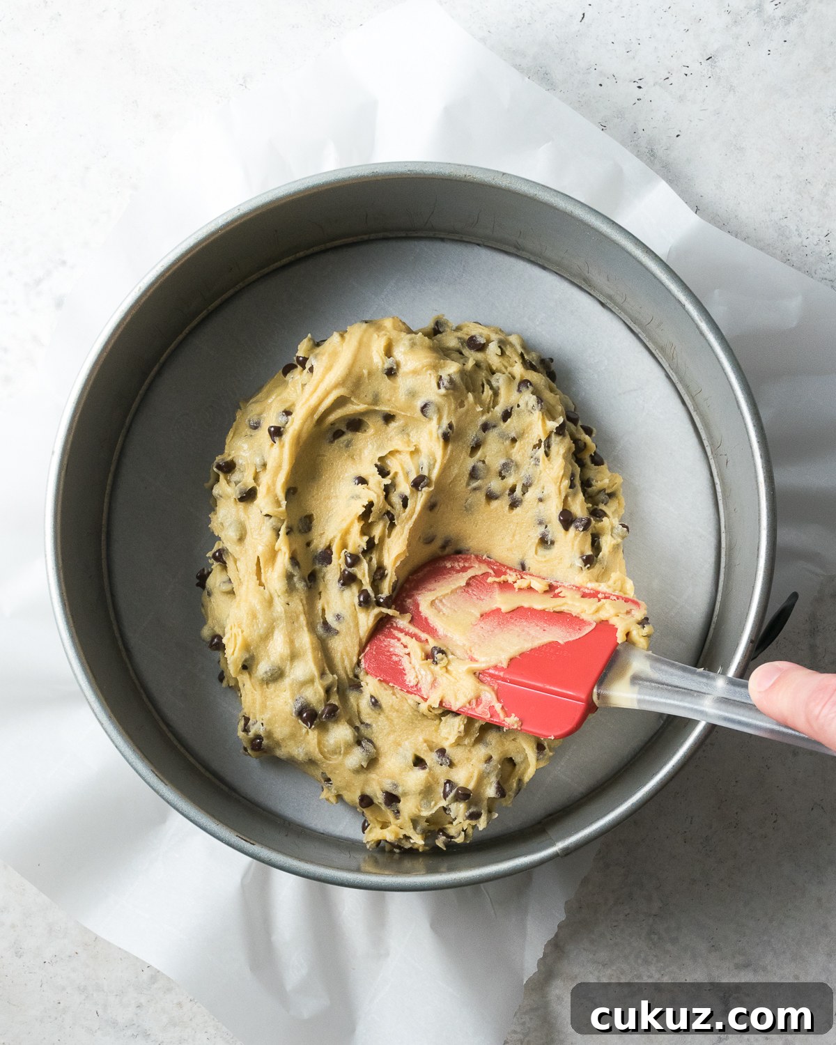 Cookie dough being spread into a large pan to make a cookie cake.