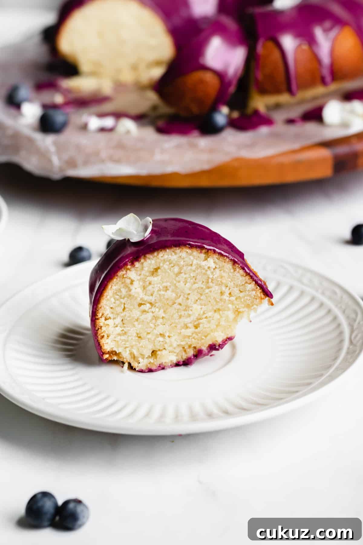 Close up straight on shot of a piece of lemon pound cake with blueberry glaze on a plate.