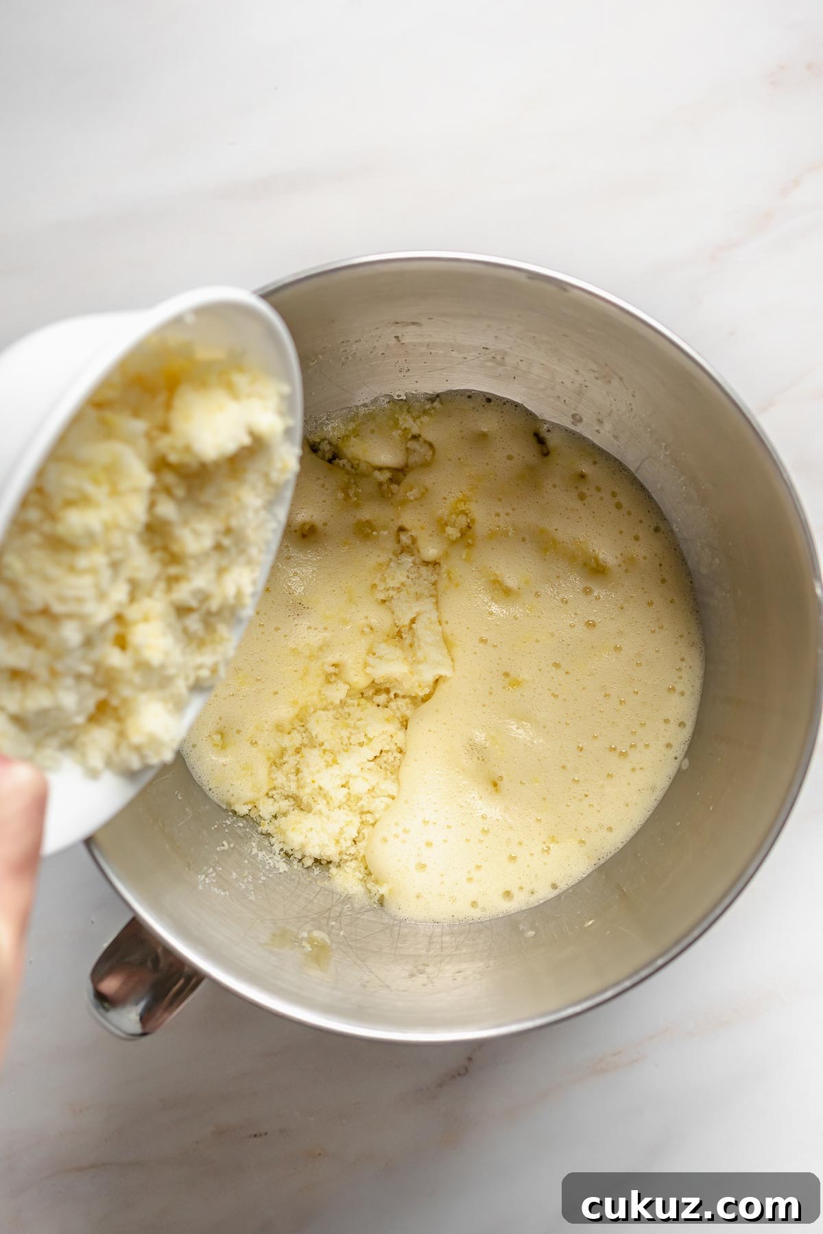 Lemon zest sugar pouring into whipped eggs.