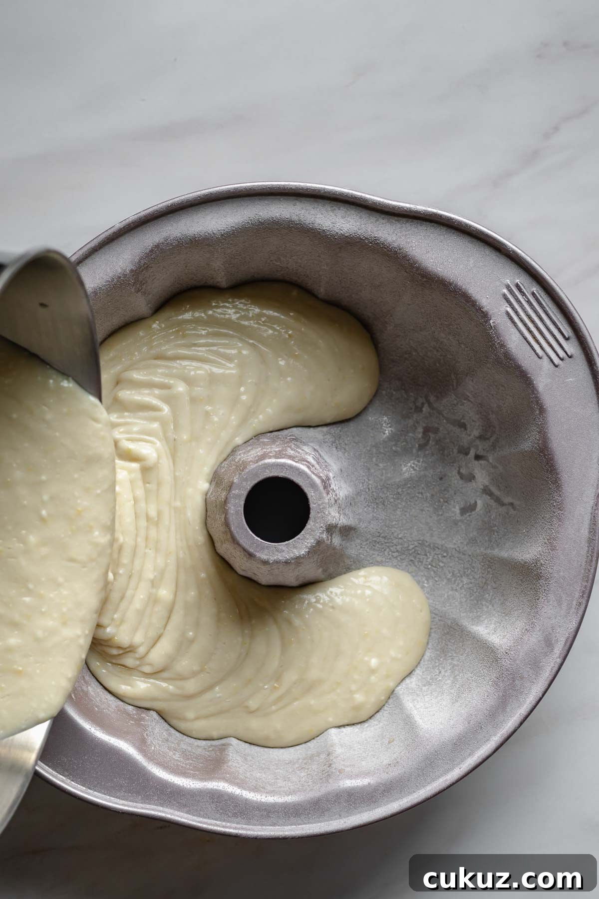 Lemon ricotta cake batter pouring into a prepared bundt pan.