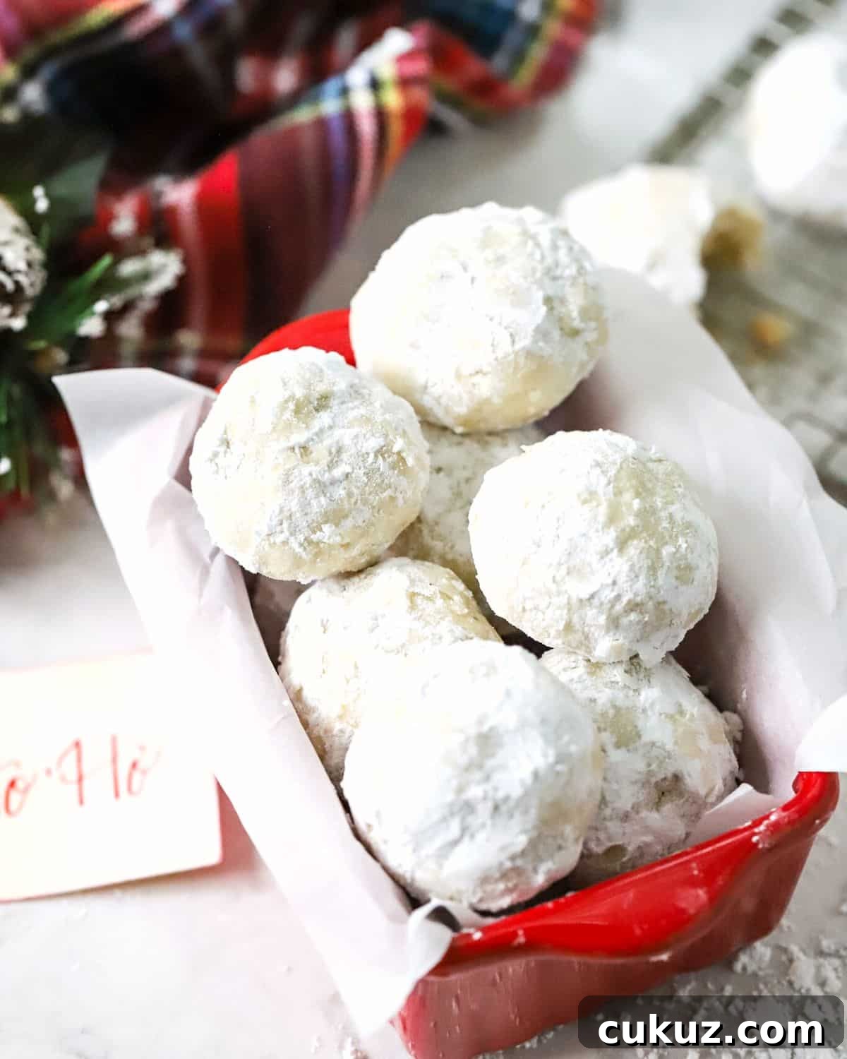 Classic Snowball Cookies Recipe for Perfect Holiday Cookies 7 Snowball cookies stacked in a red dish lined with parchment paper.