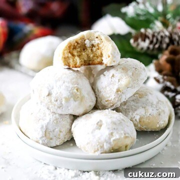 Classic Snowball Cookies Recipe for Perfect Holiday Cookies 9 Snowball cookies rolled in powdered sugar stacked on a white plate.