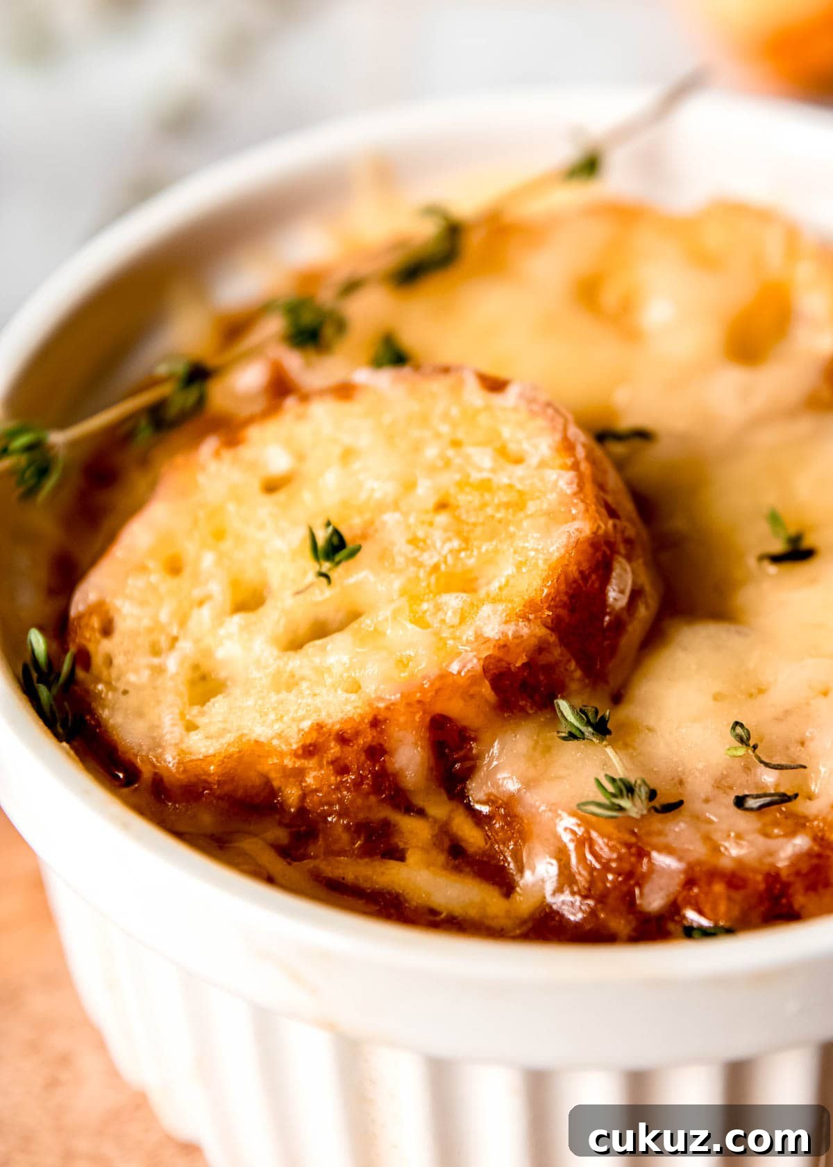 closeup view of a white ramekin full of French Onion Chicken Soup topped with melty gruyere, toasted baguette, and fresh thyme
