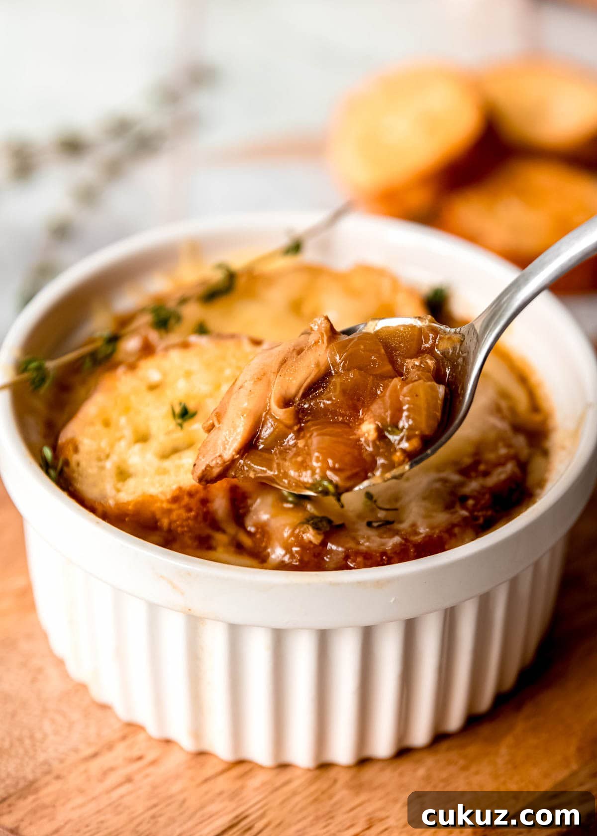 A spoonful of French Onion Chicken Soup over a ramekin full of toasted baguette, melty gruyere, and creamy soup.