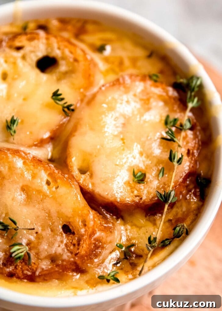 closeup view of golden brown cheese over toasted baguette on a bowl of french onion chicken soup