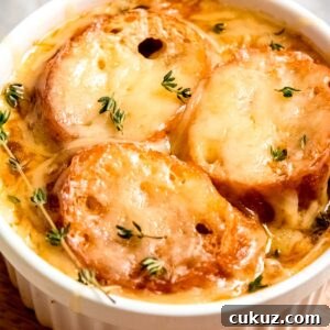 overhead closeup view of white ramekin filled to the brim with french onion chicken soup, toasted baguettes, and melted gruyere cheese