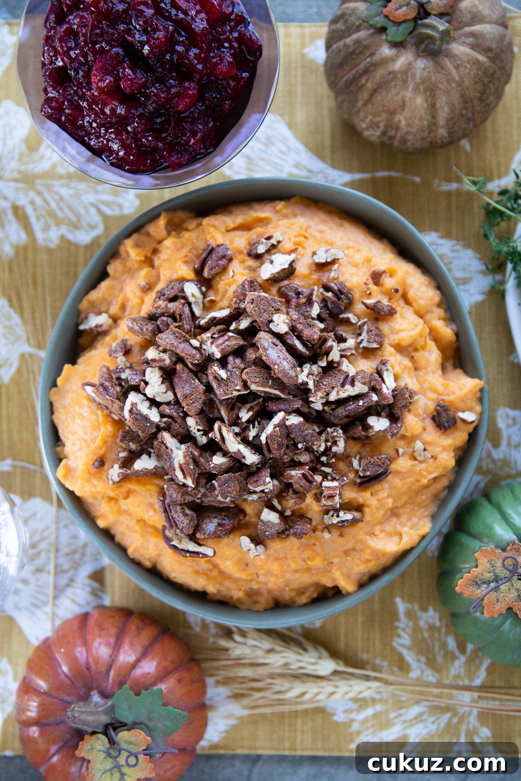 Mashed Sweet Potatoes with Cinnamon-Spiced Pecans 2 Mashed Sweet Potatoes with Spiced Pecans in a green bowl on a table with cranberry sauce and a gold pumpkin.