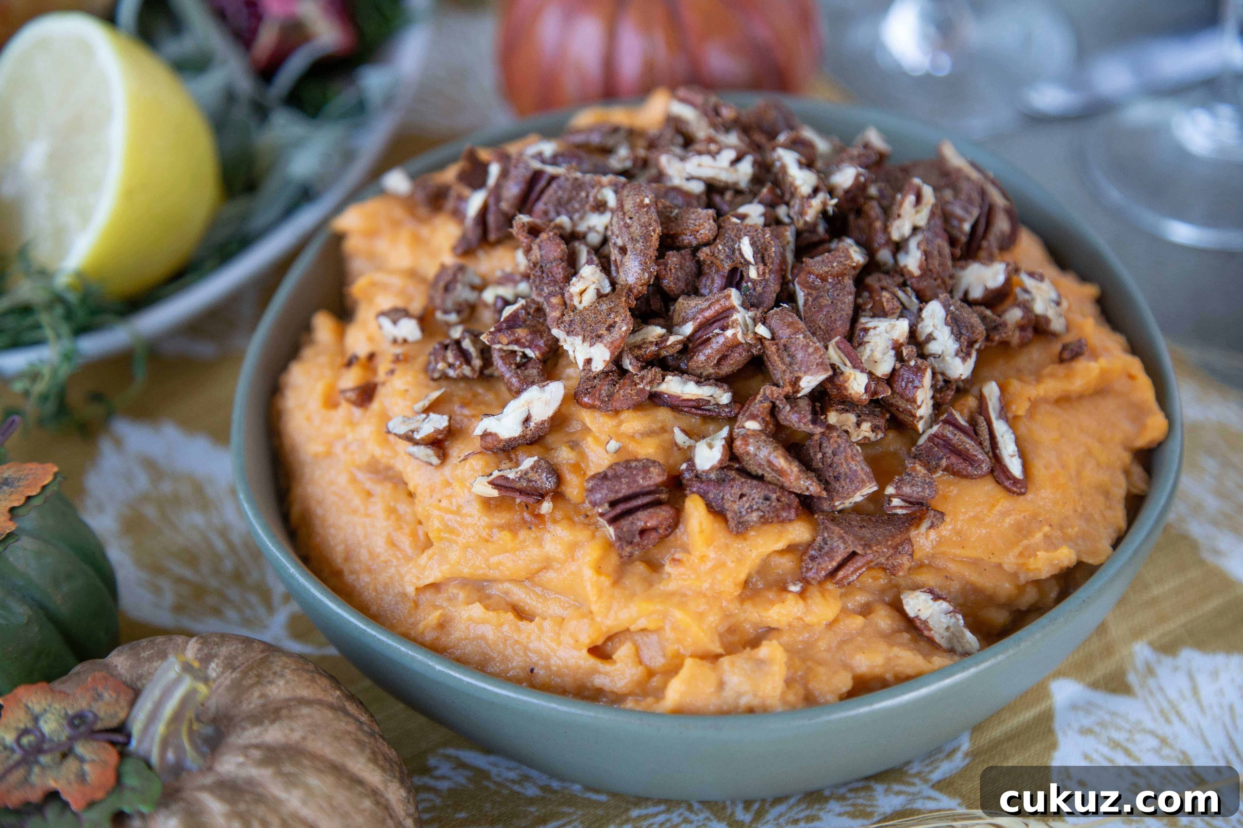 Mashed Sweet Potatoes with Cinnamon-Spiced Pecans 4 Mashed Sweet Potatoes with Spiced Pecans in a green bowl on a table with gold, green, and orange faux pumpkins.
