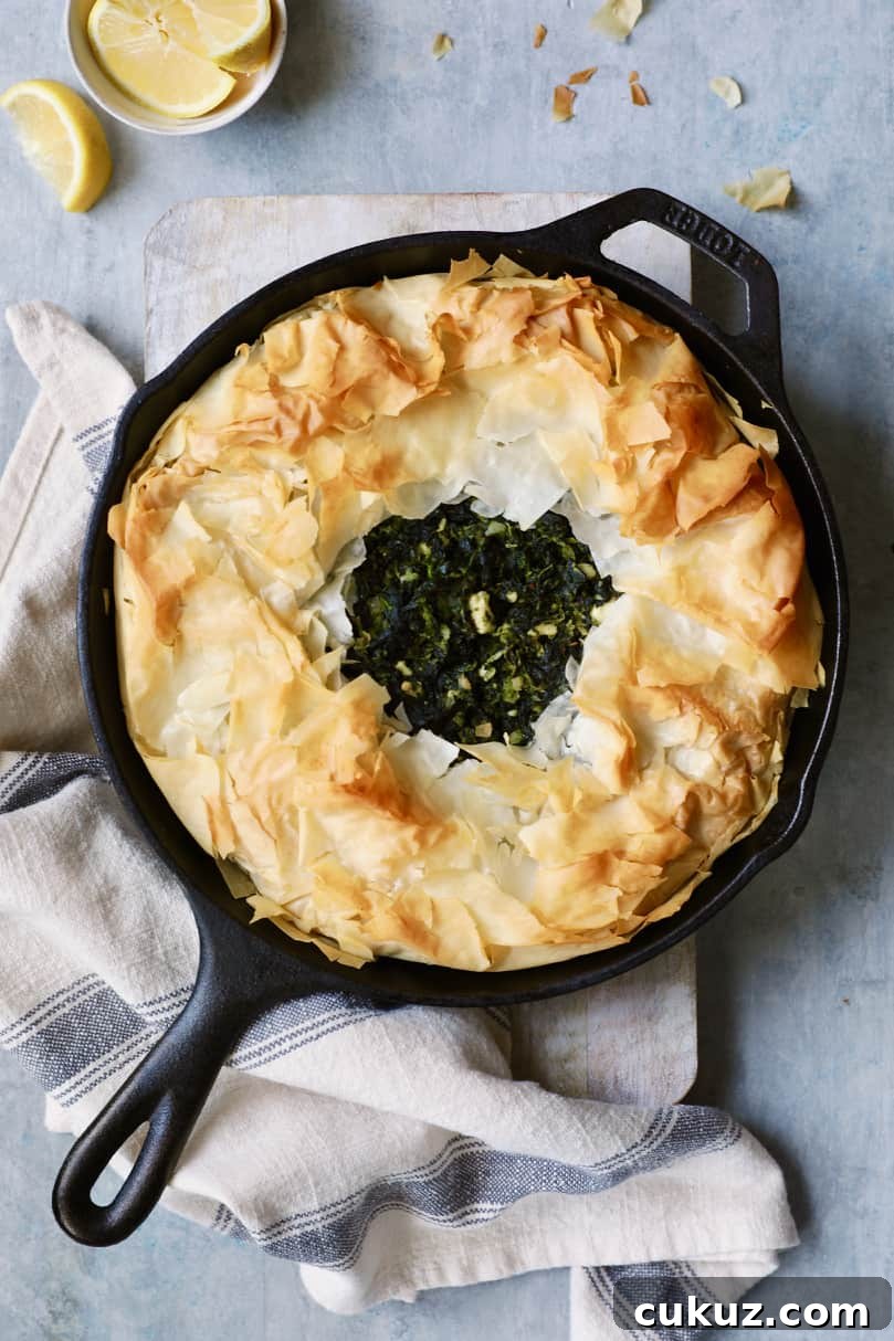 Photo of Skillet Spanakopita (Greek Spinach and Feta Pie) on cutting board after being baked with gray striped towel.
