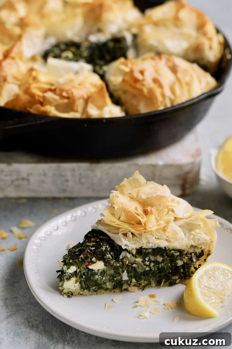 Photo of one slice of Skillet Spanakopita (Greek Spinach and Feta Pie) on small white plate with rest of the pie in the background.