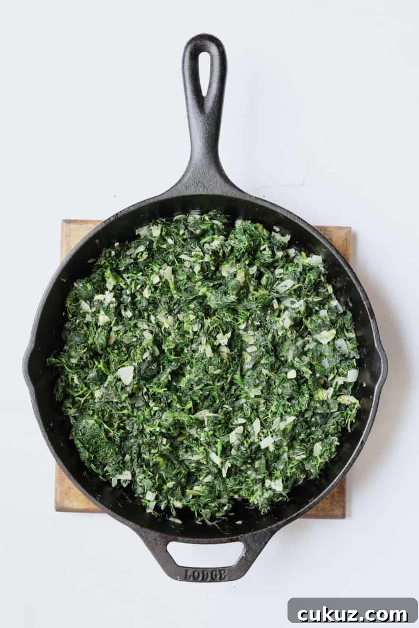 Photo of spinach and onions being cooked in cast iron skillet.
