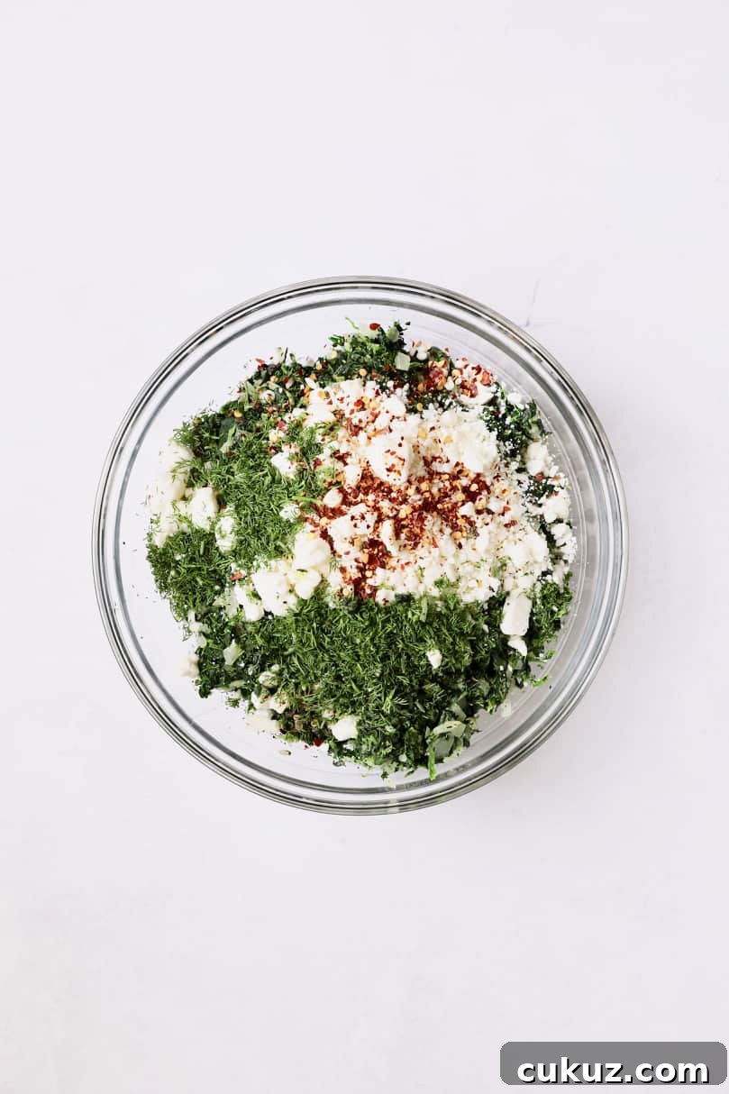 Photo of ingredients for spanakopita combined in glass bowl.