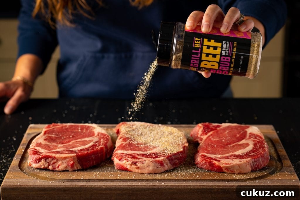 Three steaks being seasoned with Hey Grill Hey Beef Rub.
