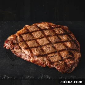 A steak with grill marks on a black surface.