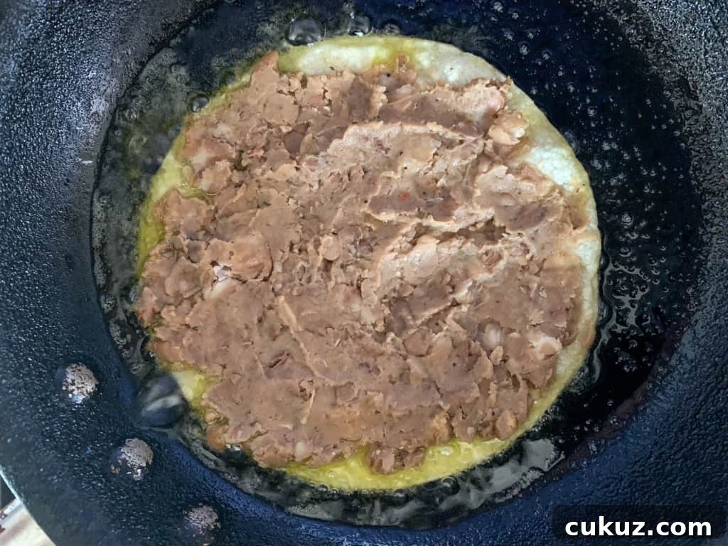 A corn tortilla spread with beans frying in a frying pan. 