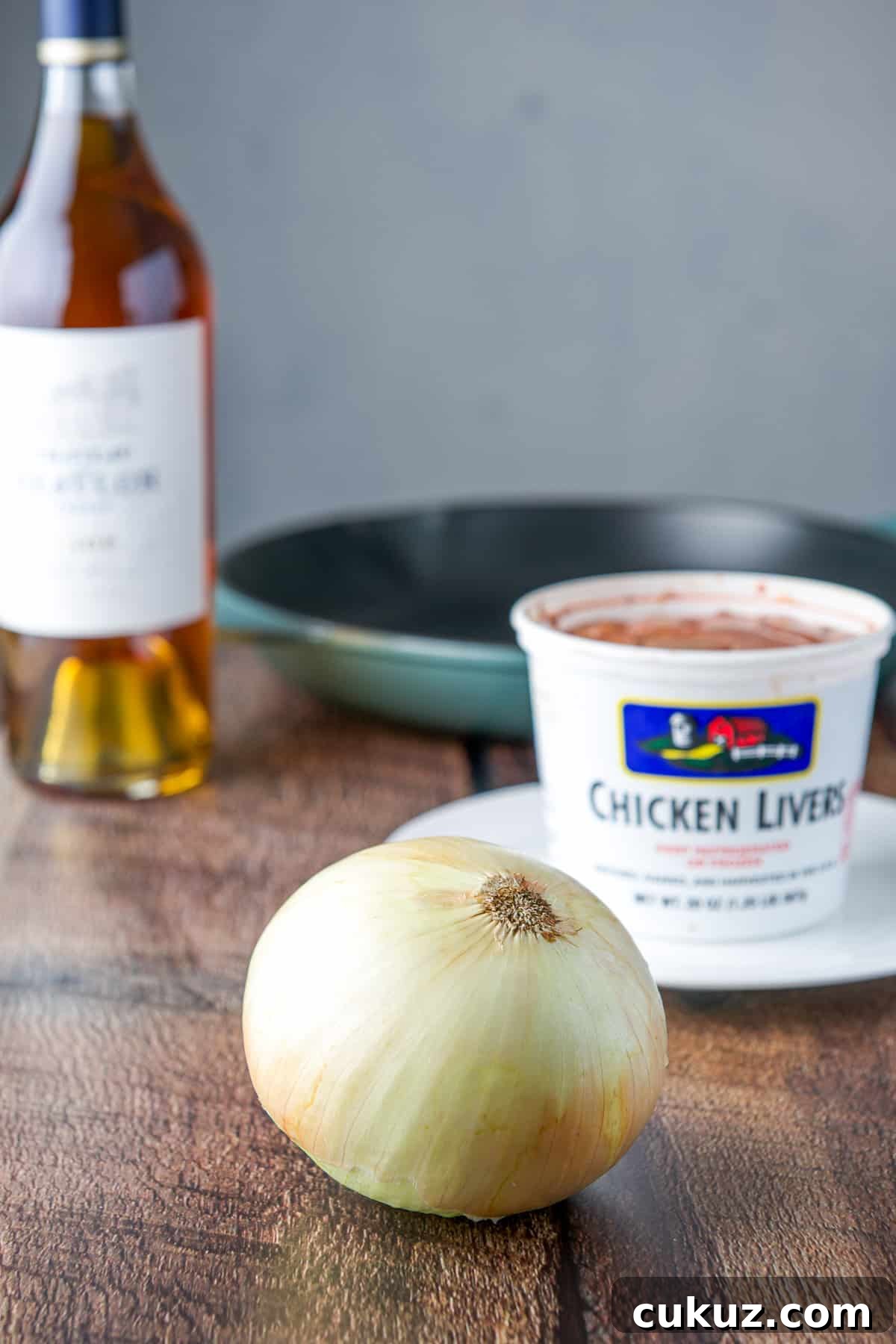 Onion, livers, cognac and a pan on a table.