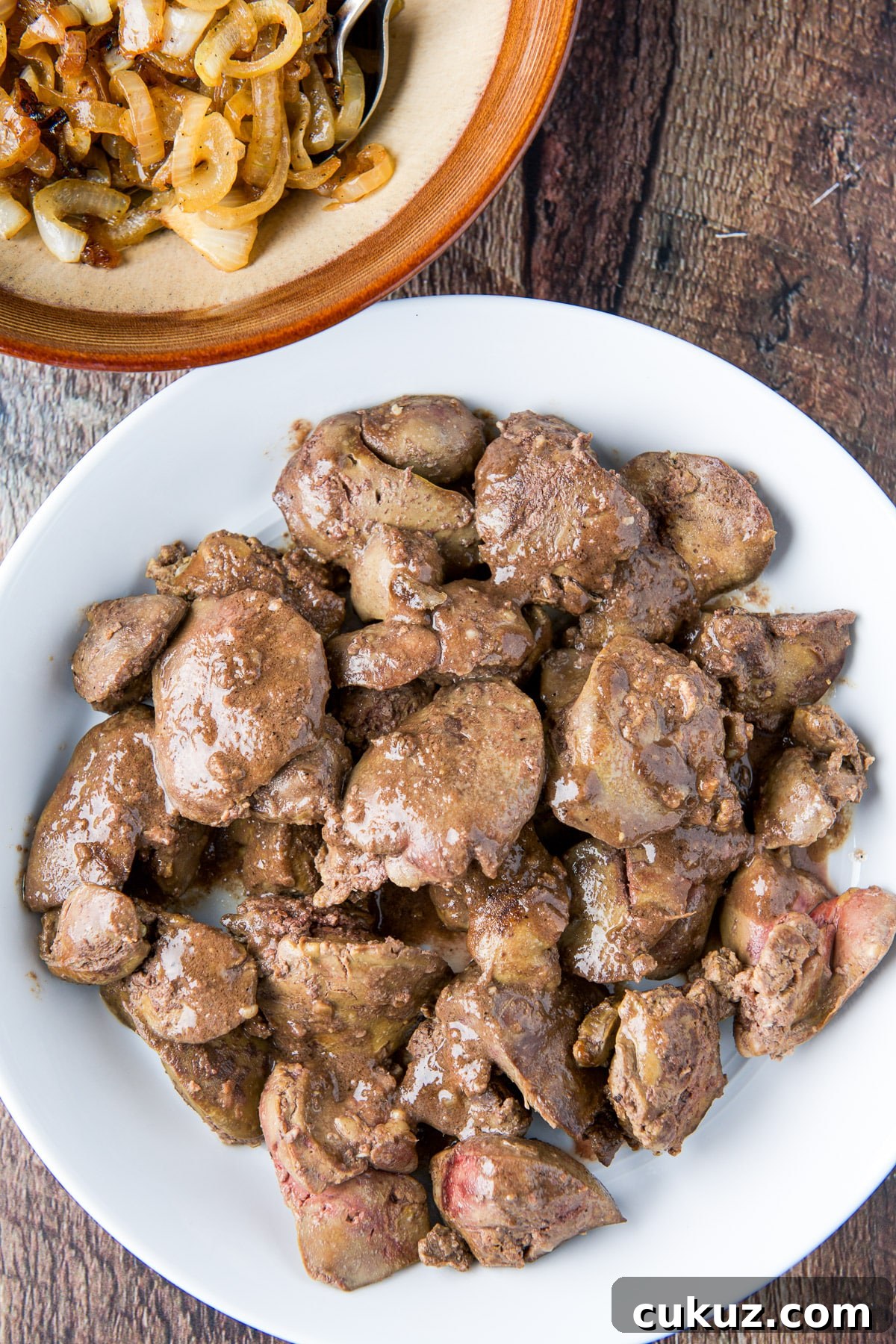 Overhead view of a white plate of livers and bowl of onions