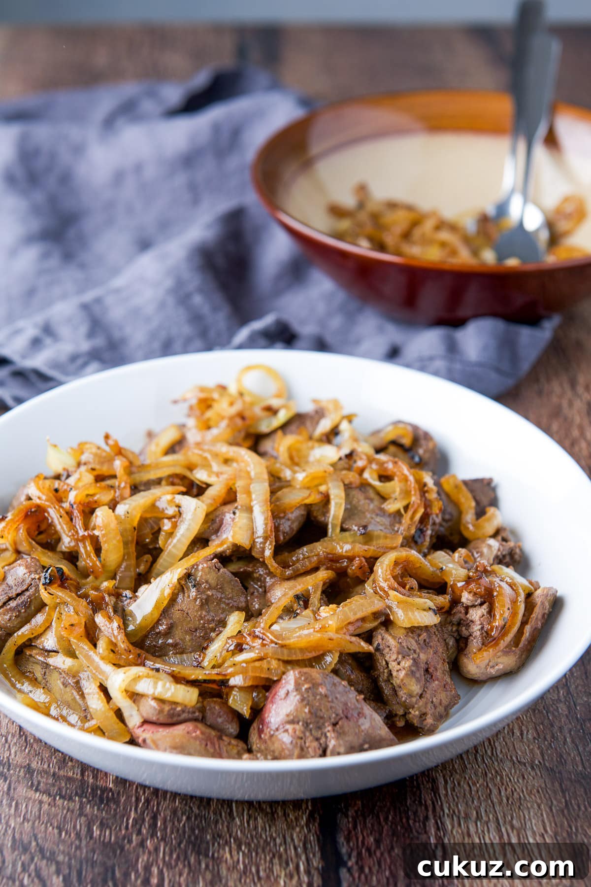 A wood table with a bowl of onions behind a white plate of livers and onions