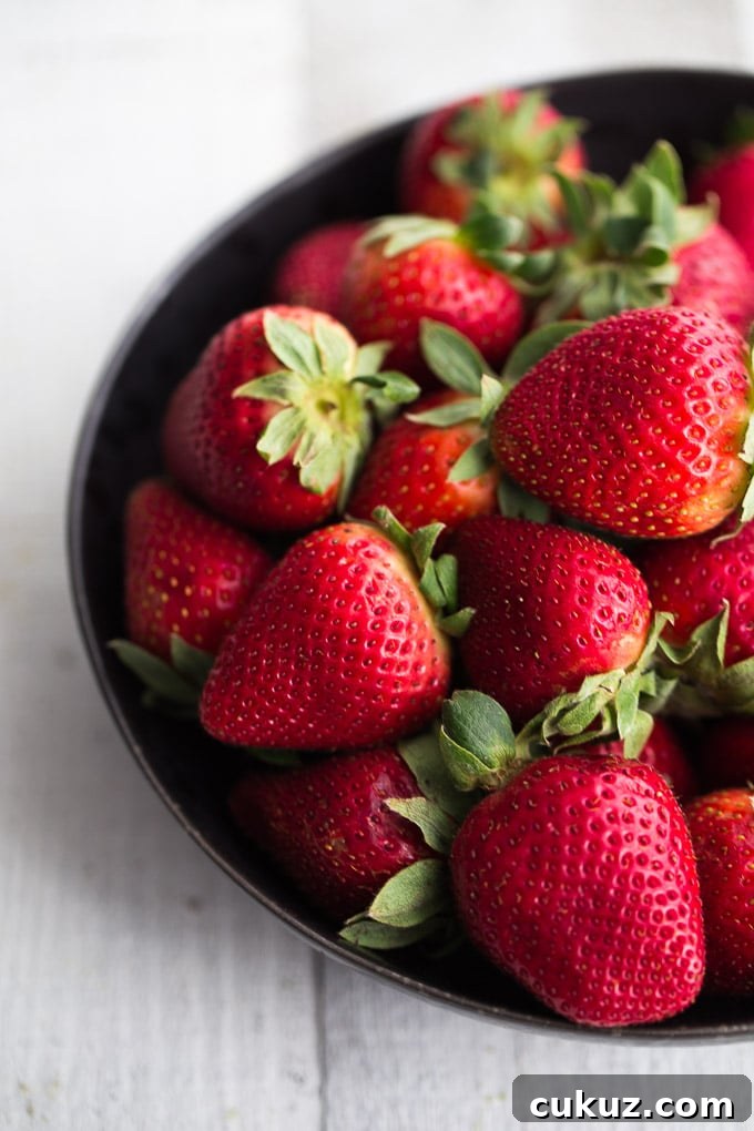 Fresh strawberries in a black bowl on a white surface.