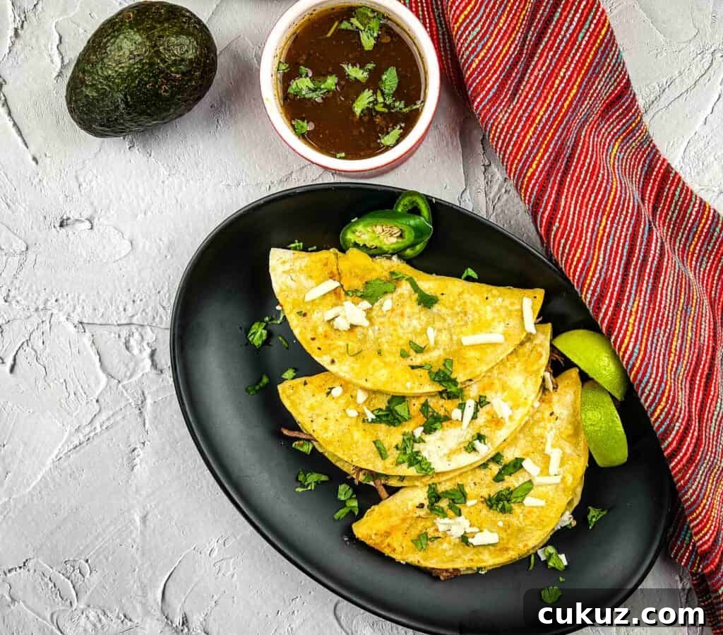 Birria Tacos Recipe with Dipping Consomme 6 birria tacos and broth on a black plate