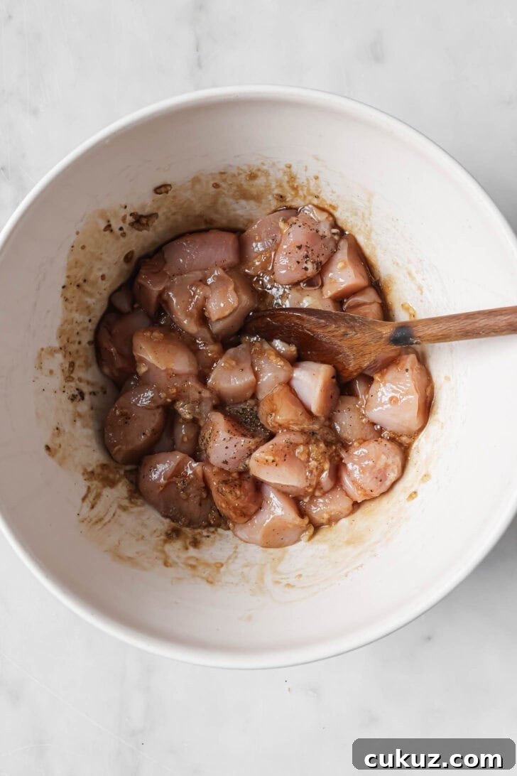 Chicken mixed with marinade ingredients in a bowl with a wooden spoon.