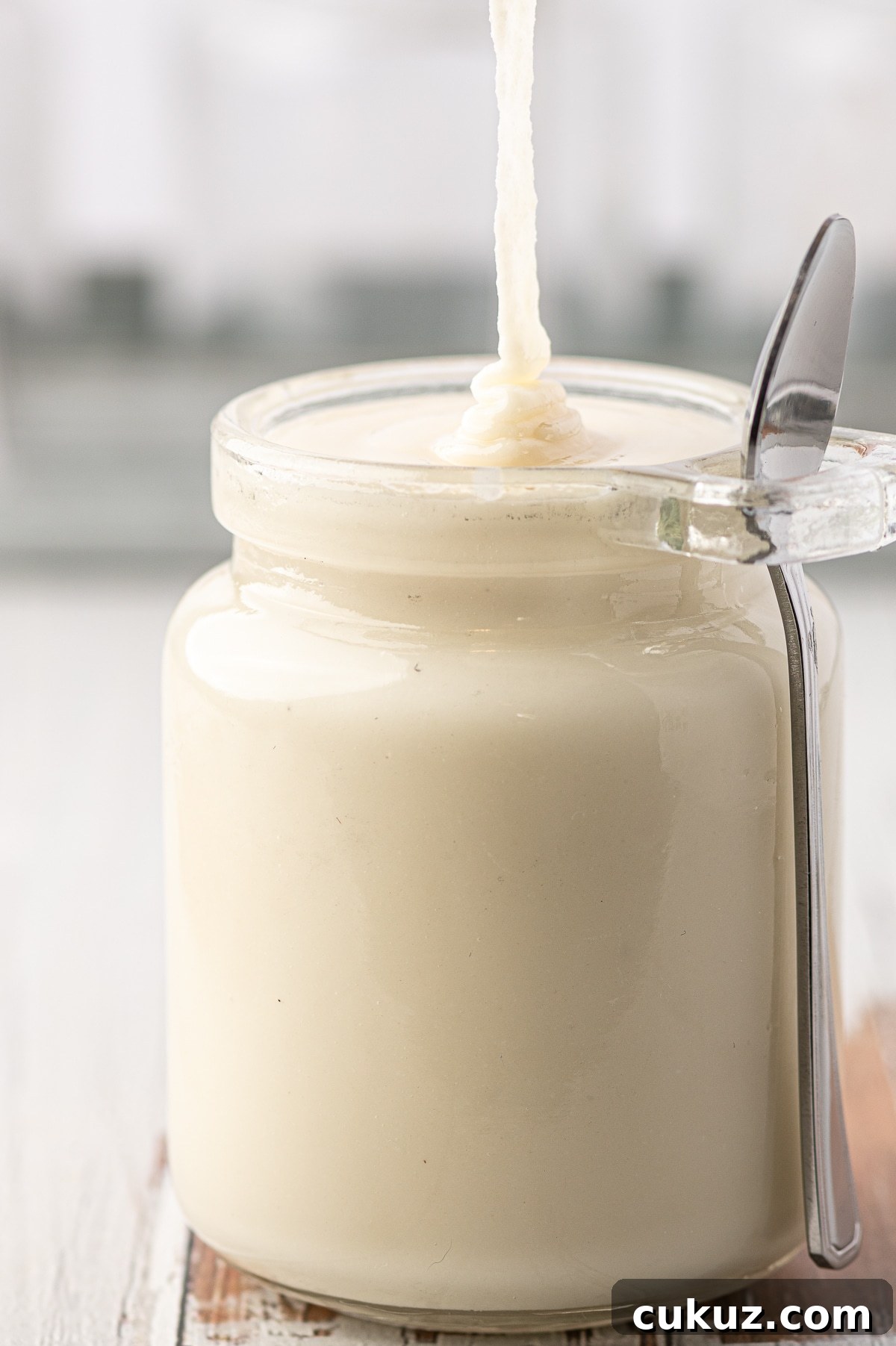 Just made low carb coconut butter being poured into a glass jar against a grey background 