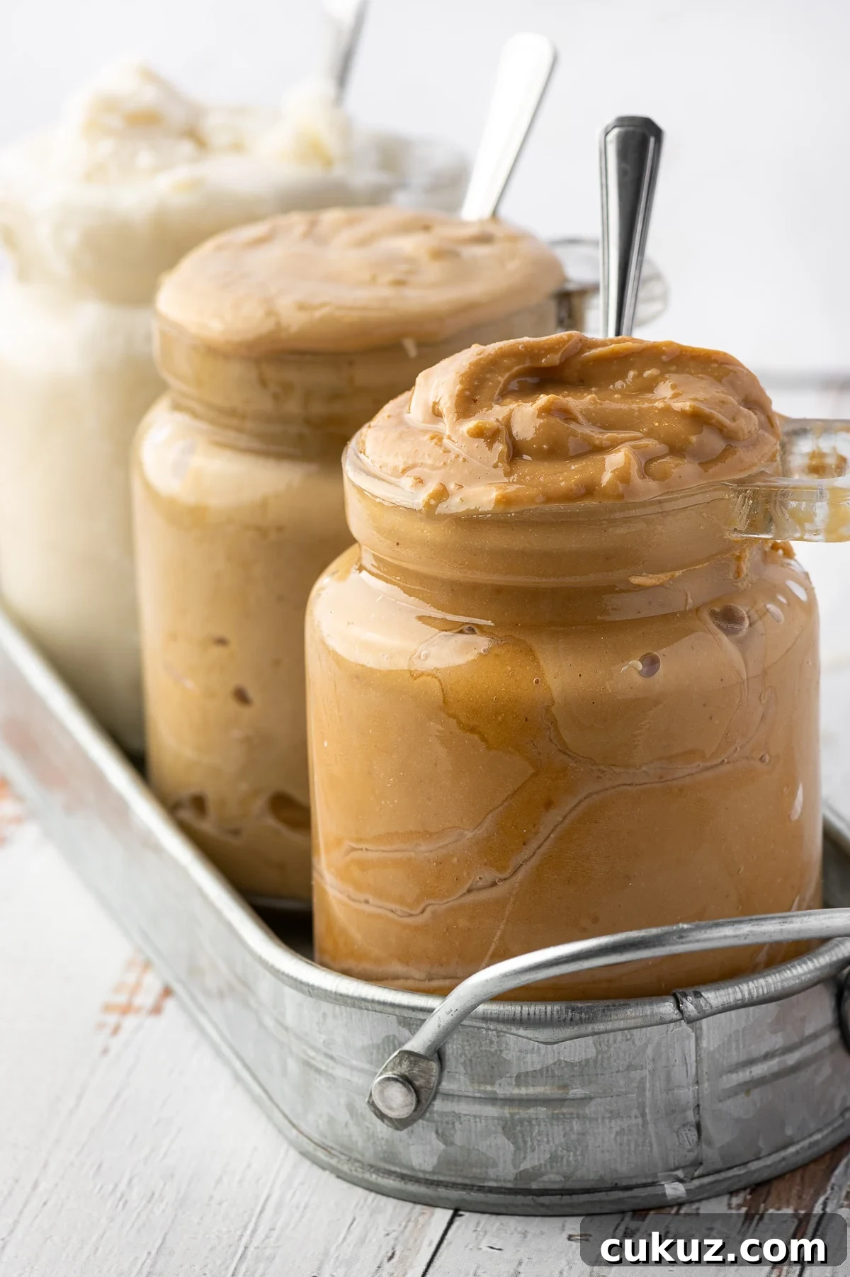 Three overflowing jars of nut butters in a metal jar against a bright white background 