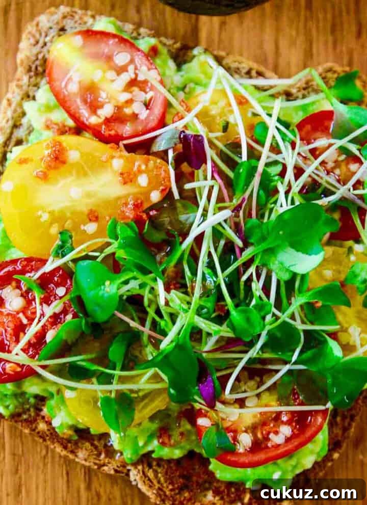 A close up photo of a slice of avocado toast topped with small heirloom tomatoes and microgreens.