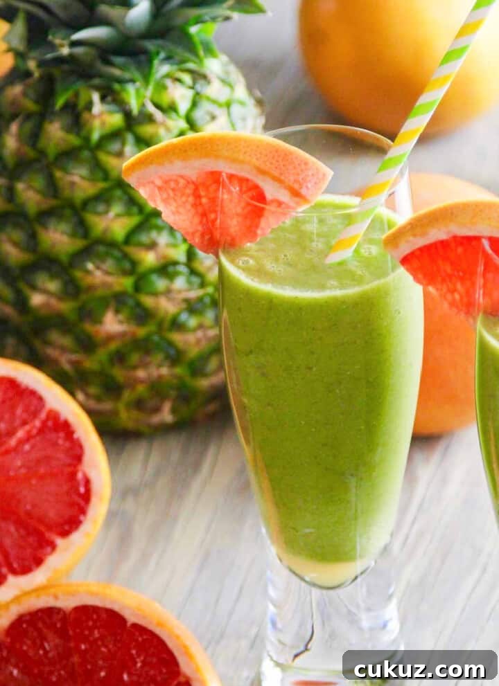 Two glasses of a green smoothie recipe garnished with grapefruit slices and straws.