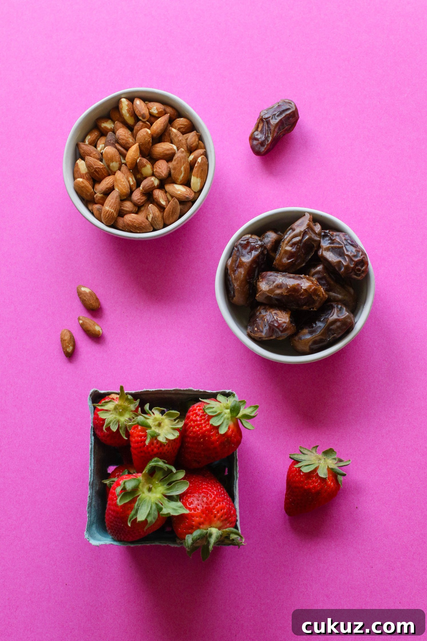 bowl of raw almonds, Medjool dates, and strawberries on pink paper by Flora & Vino