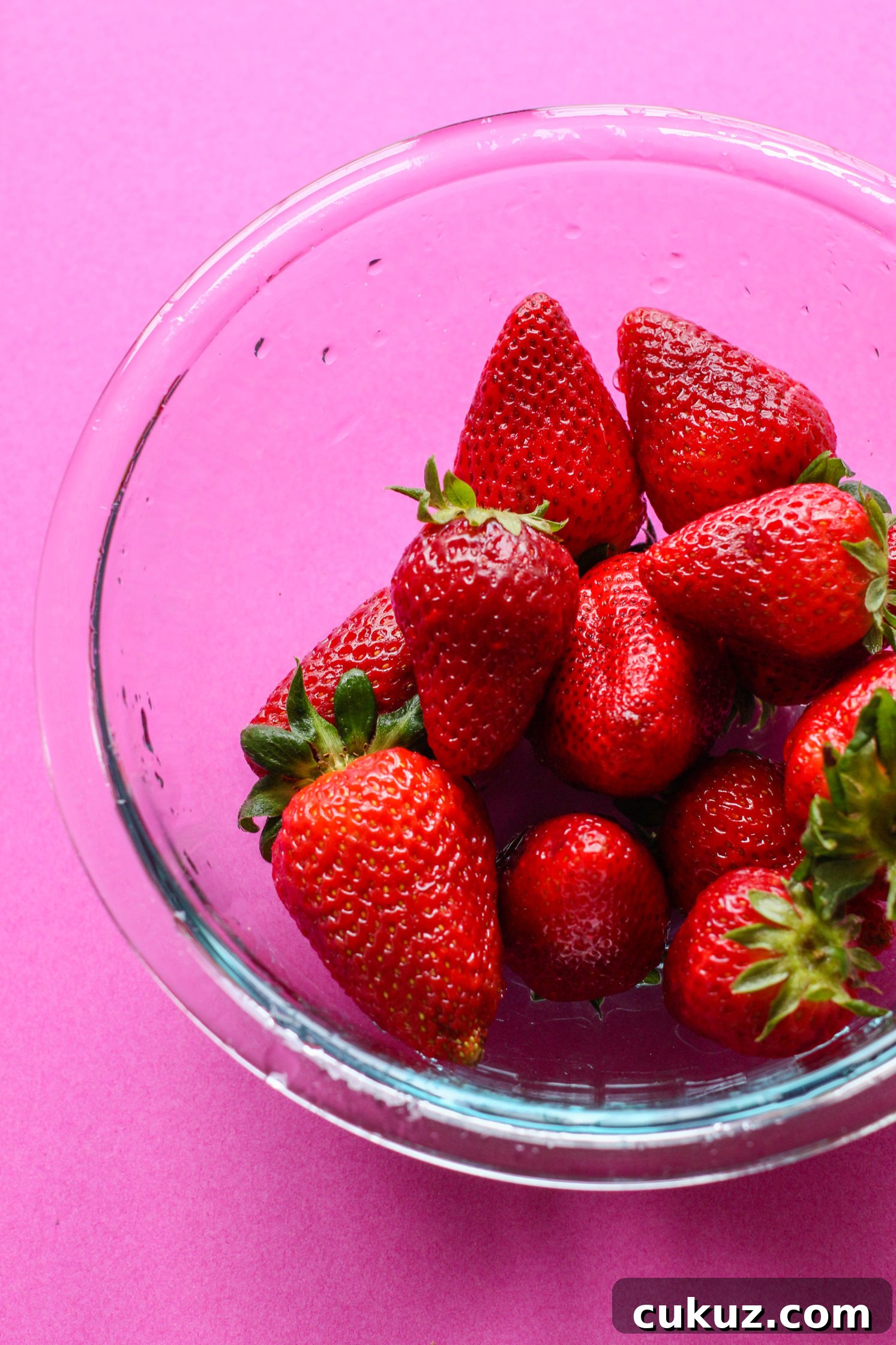 raw strawberries in bowl on pink background by Flora & Vino