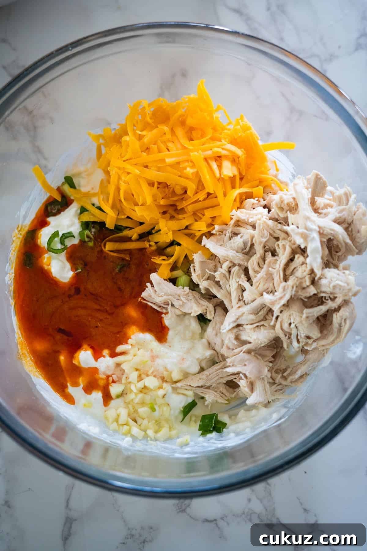 The ingredients for a buffalo chicken taco salad in a glass bowl.