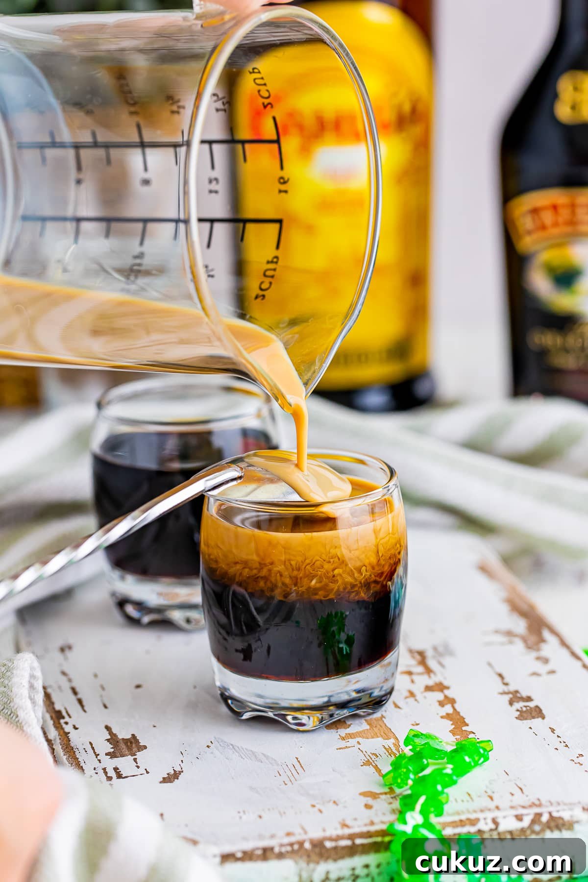 How to Make a Baby Guinness Shot: Creamy Espresso Liqueur Cocktail 6 Showing how to invert spoon over the top of the Baby Guinness and slowly pour the Bailey's Irish Cream on top. Shown on a white chipped wooden serving board