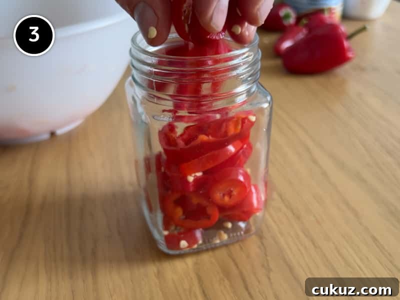 Placing chopped red chillies into a glass jar.