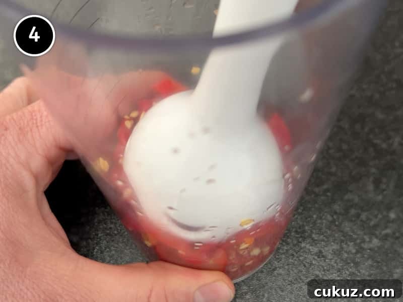 Blending red shatta sauce with an immersion blender