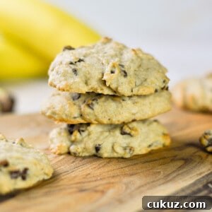 three banana bread chocolate chip cookies stacked on a cutting board.