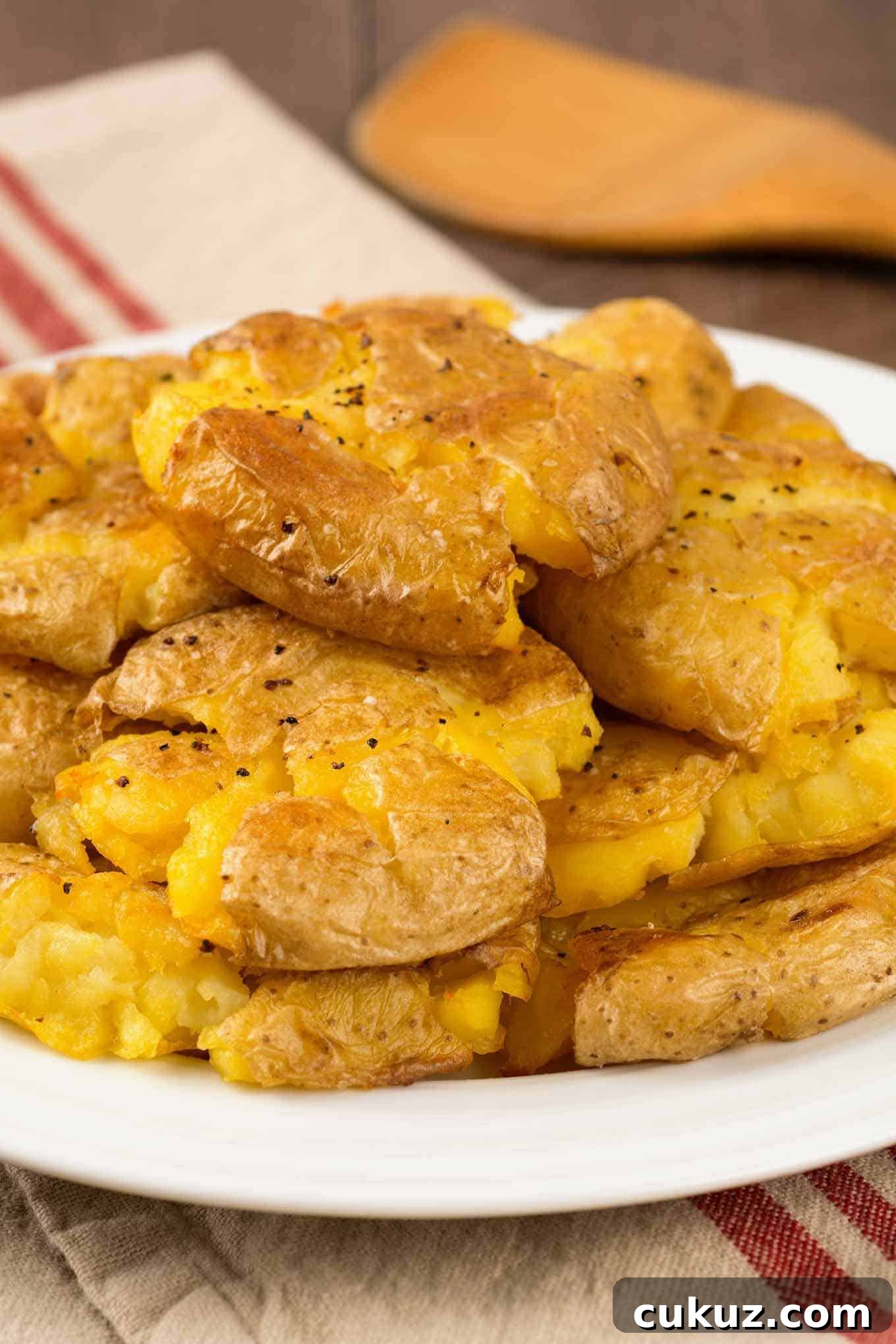 A stack of golden, crispy smashed potatoes on a white plate, seasoned with salt and pepper.