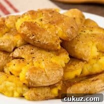 A stack of golden, crispy smashed potatoes on a white plate, seasoned with salt and pepper.