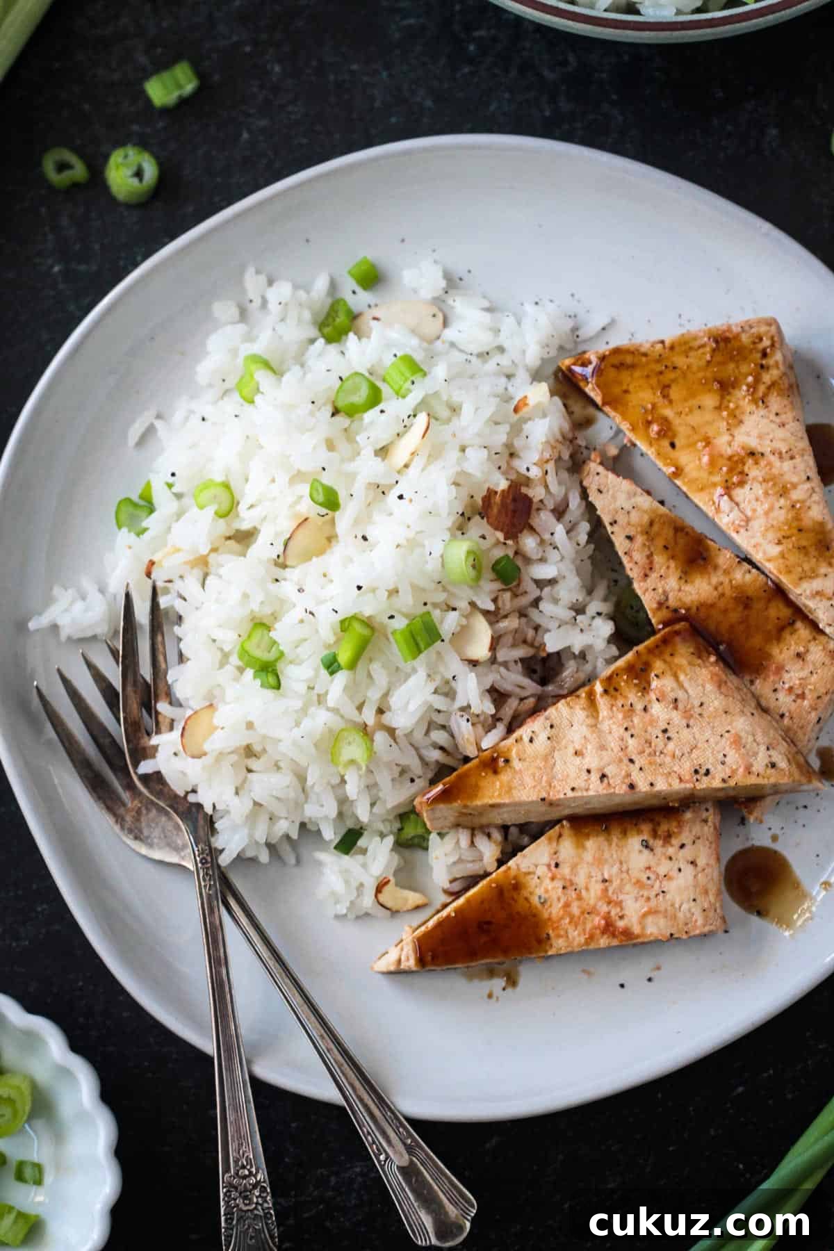 Coconut rice on a plate with triangles of baked tofu and two forks.