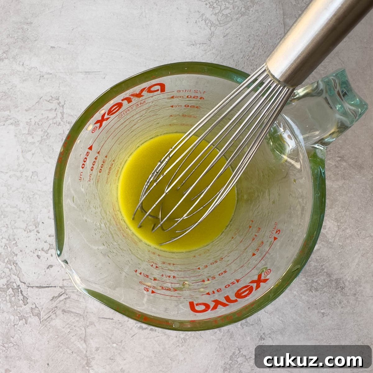 Whisking golden colored vinaigrette in a glass measuring cup.