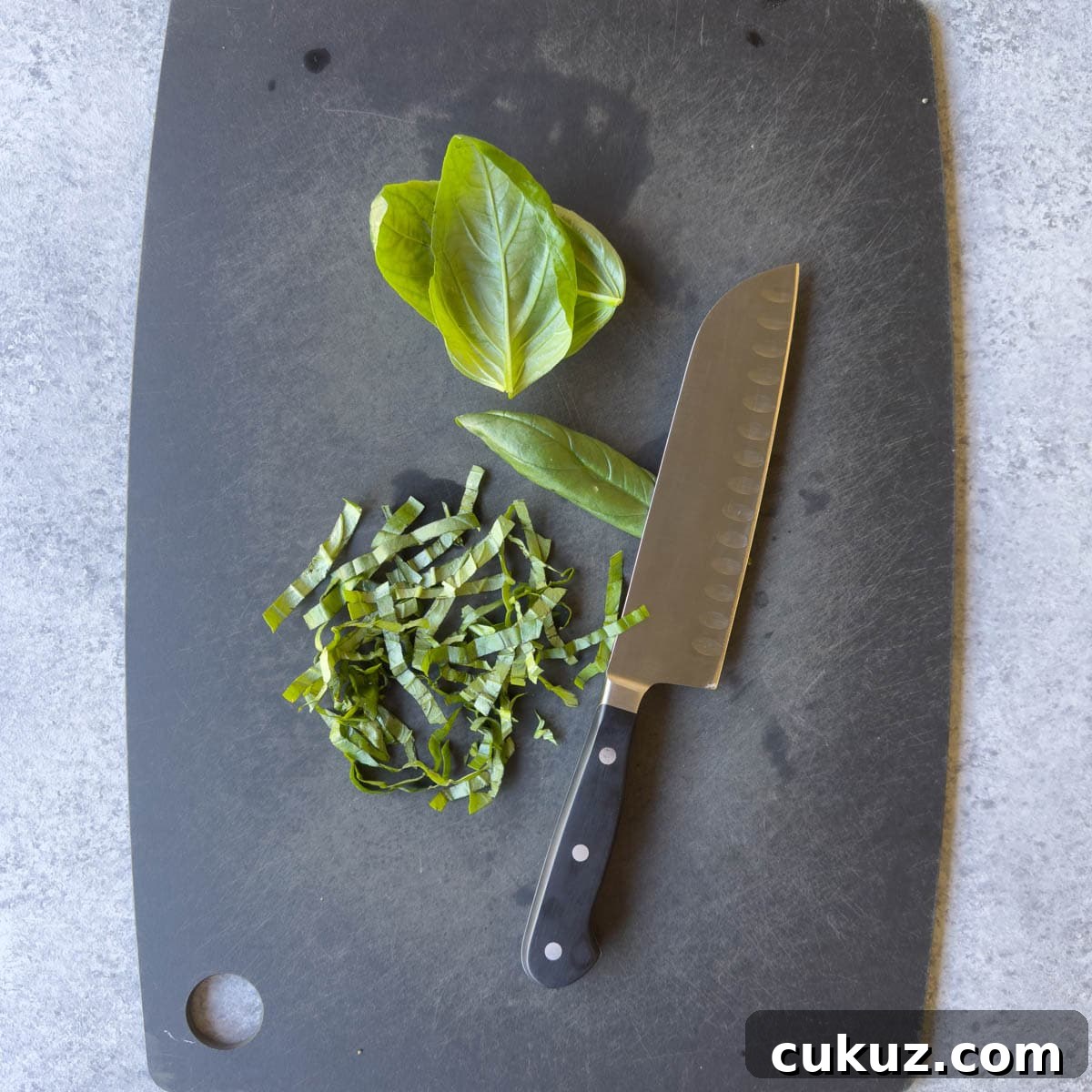 Bright green basil leaves on a black cutting board.