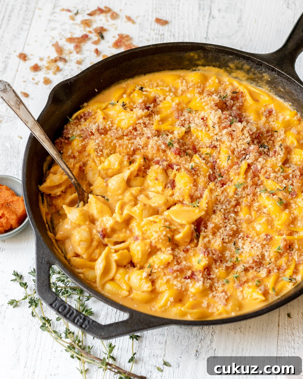 macaroni pasta in a cast iron skillet in a pumpkin cheddar cheese sauce topped with bacon panko breadcrumbs. 