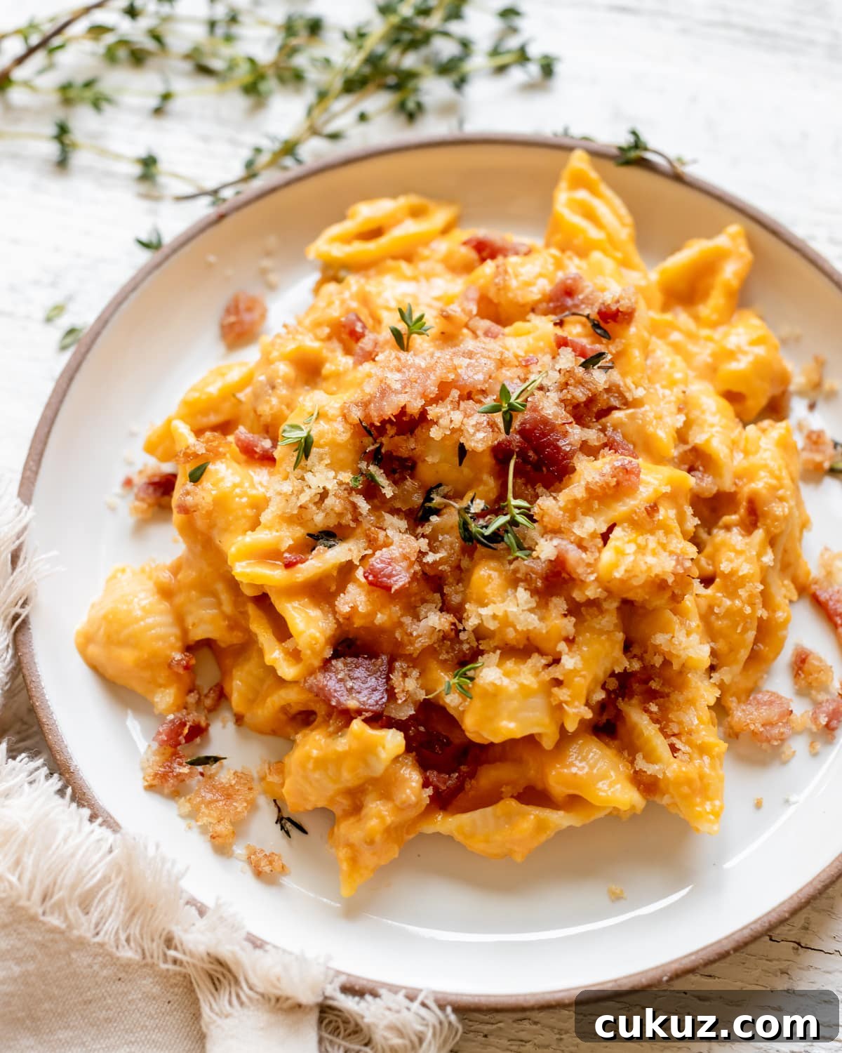macaroni pasta on a white plate in a pumpkin cheddar cheese sauce garnished with bacon and fresh thyme. 