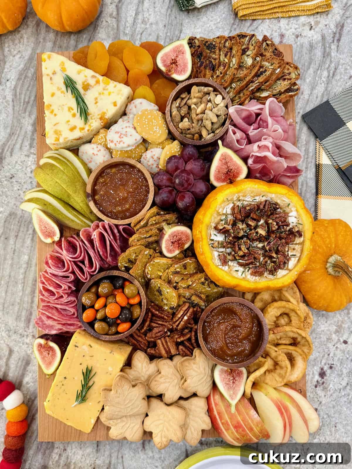 A rectangular wooden food board filled with autumnal snacks like cheese, salami, sliced pear and a pumpkin dip.