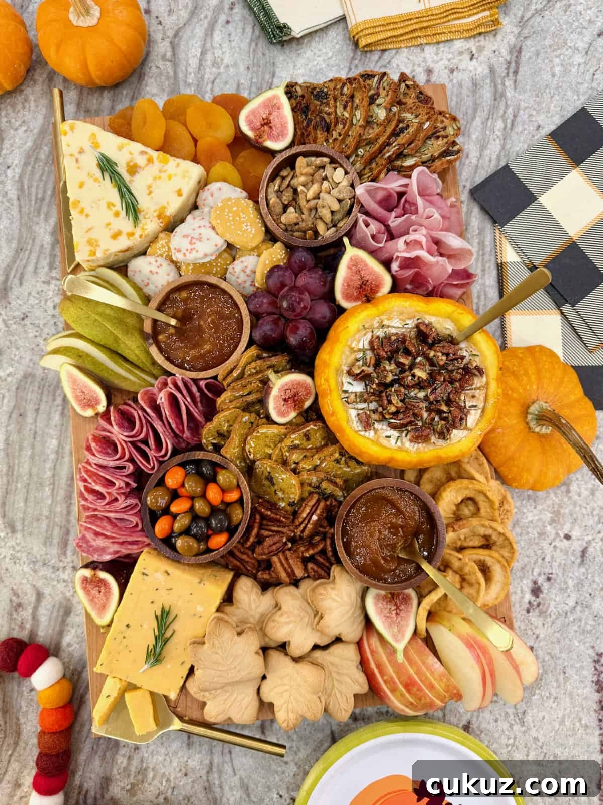 A rectangular wooden food board filled with autumnal snacks like cheese, salami, sliced pear and a pumpkin dip.