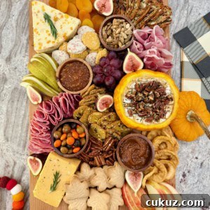 A rectangular wooden food board filled with autumnal snacks like cheese, salami, sliced pear and a pumpkin dip.