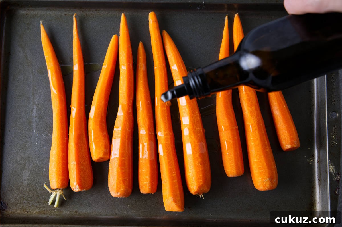 Drizzling olive oil over carrots in a sheet pan.