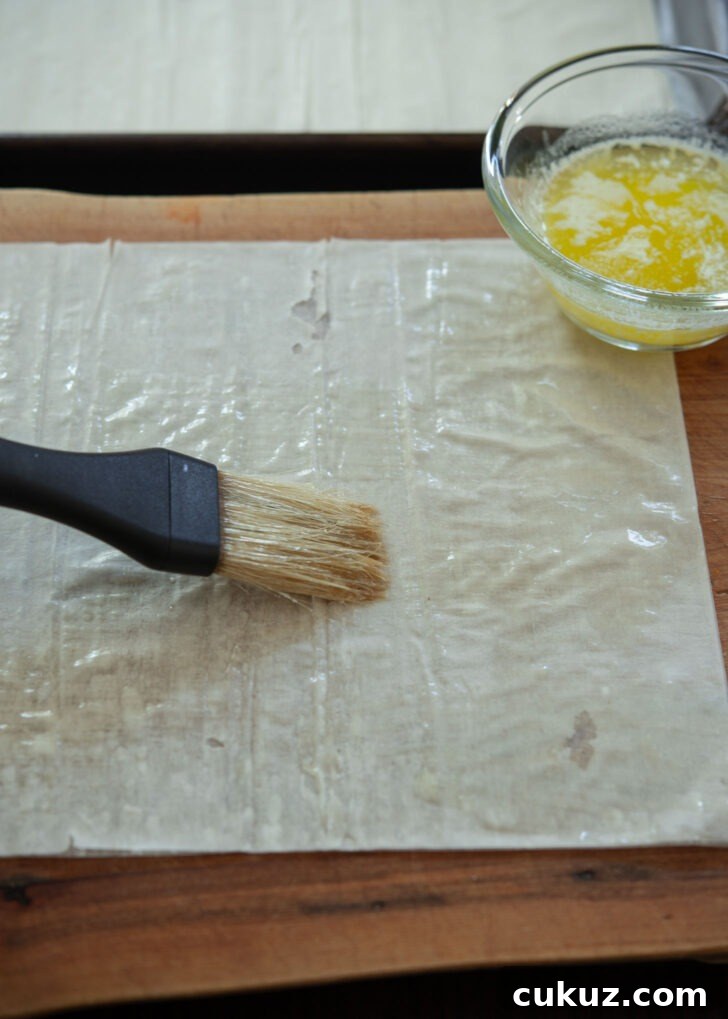A pastry brush applying melted butter on filo pastry sheet.