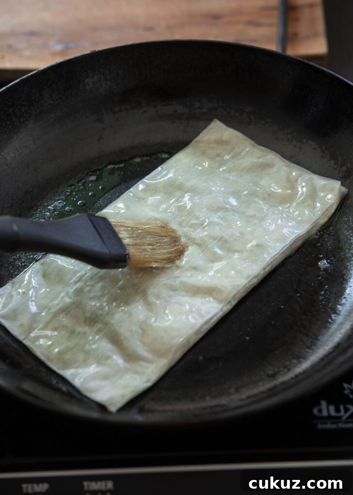 Brushing with melted butter on the top side of Katmer pastry in a skillet.